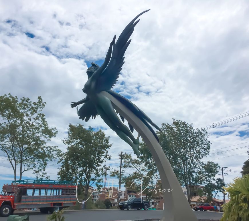 A large sculpture of a winged female with arms and wings wide open attached to a outstretched platform located at a roundabout entering El Penol- guatape