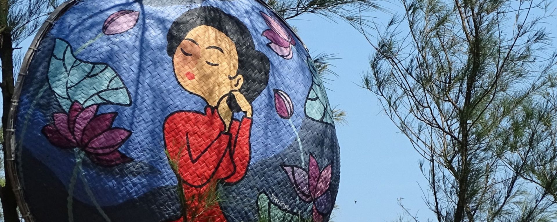 A painting of a Vietnamese women wearing a red dresspainted basket boat at Tam Thanh Mural Village