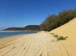A scenic view of the beach at Double Island Point, Queensland, showcasing the clear turquoise waters, sandy shoreline, and lush mountain backdrop, captured from a 4WD vehicle driving up the beach